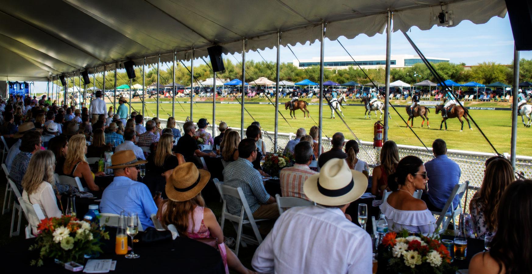 Guests watching polo from a shaded hospitality tent at the Scottsdale Polo Championships